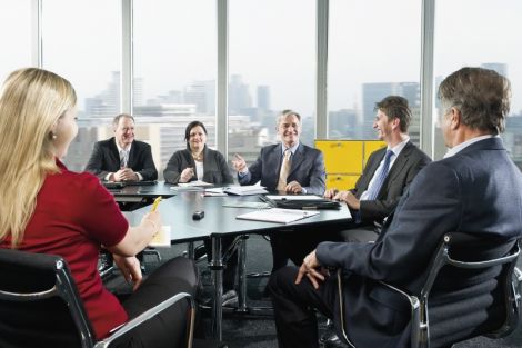 Sechs Personen sitzen um einen Tisch und kommunizieren. Auf dem Tisch befinden sich schriftliche Unterlagen.